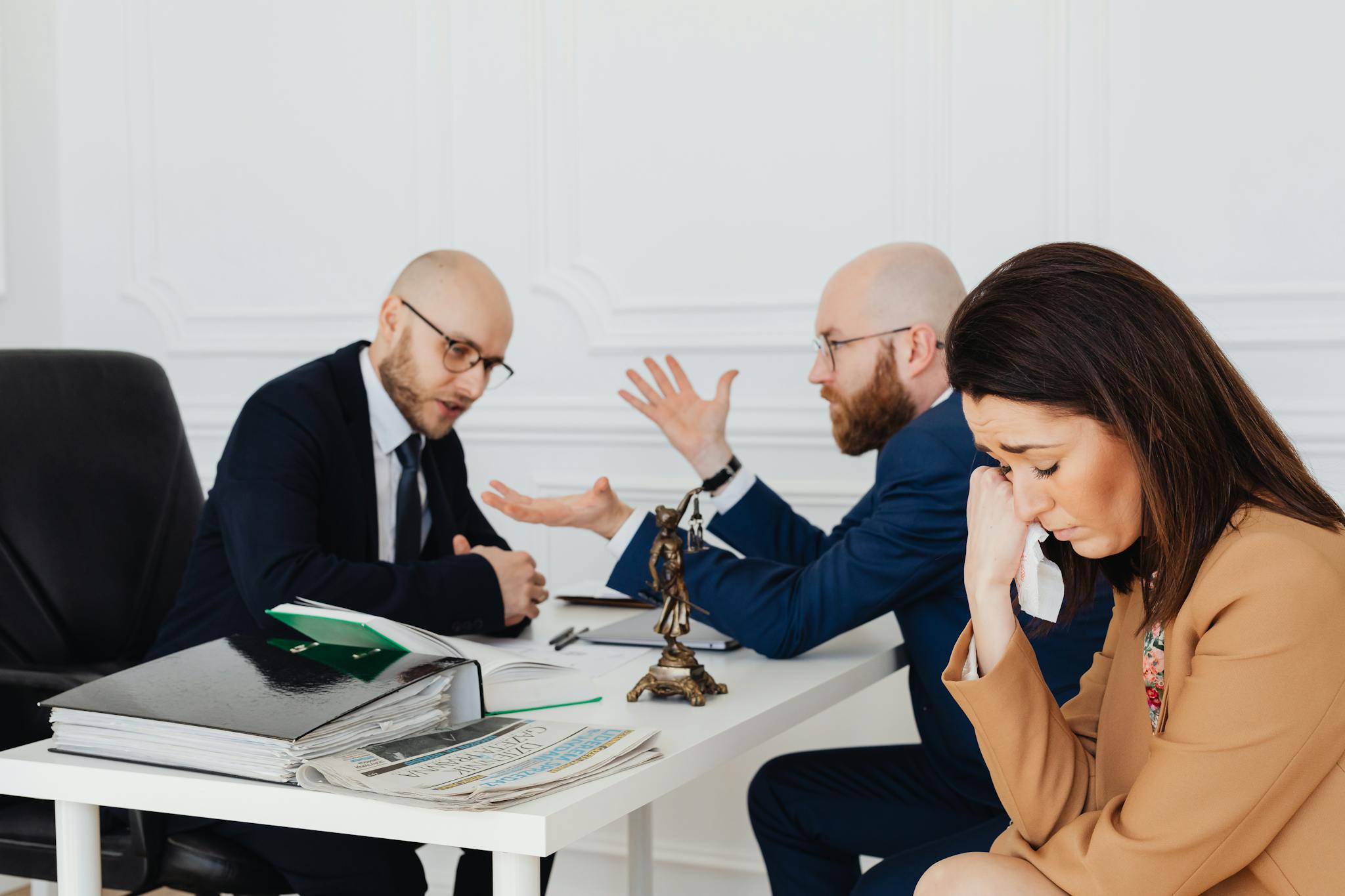 A woman appears distressed while two lawyers converse in an office.